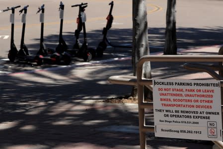 Legally parked scooters are shown near a warning sign not to park the devices on private property in San Diego, California