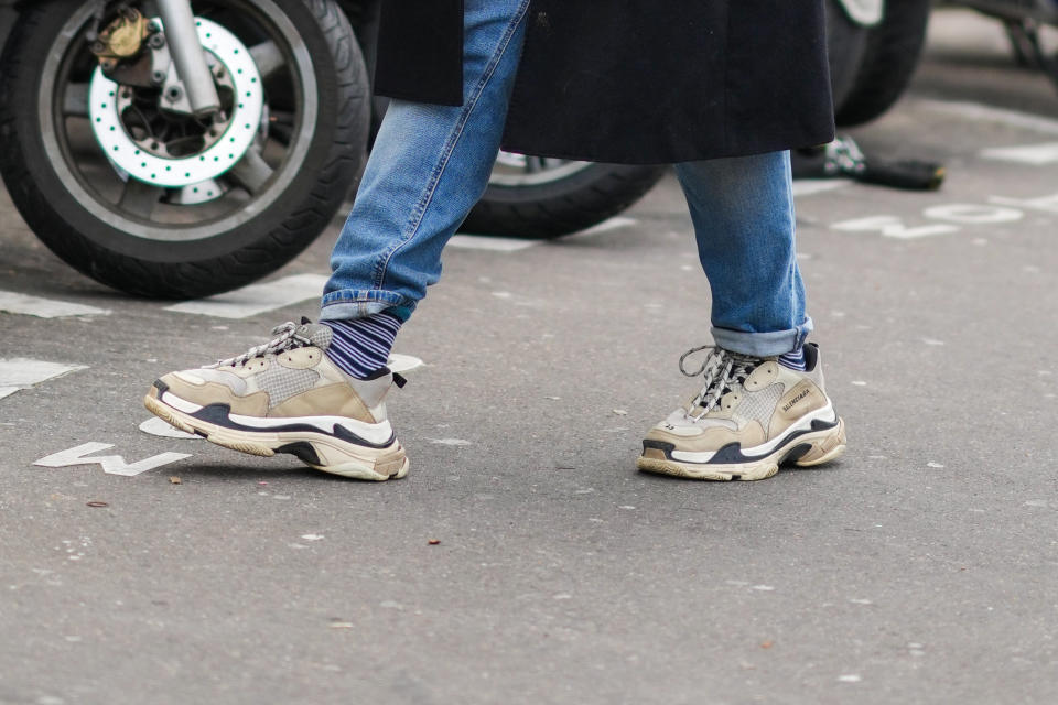 PARIS, FRANCE - JANUARY 20: A guest wears a black long coat, blue denim jeans pants, beige leather sneakers from Balanciaga, outside Rains , during Paris Fashion Week - Menswear F/W 2022-2023, on January 20, 2022 in Paris, France. (Photo by Edward Berthelot/Getty Images)