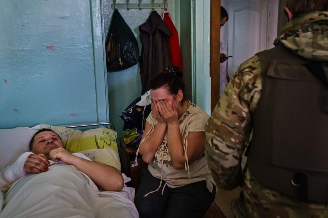 Oksana Seychuk covers her face and weeps over weeps beside her injured husband's bed.