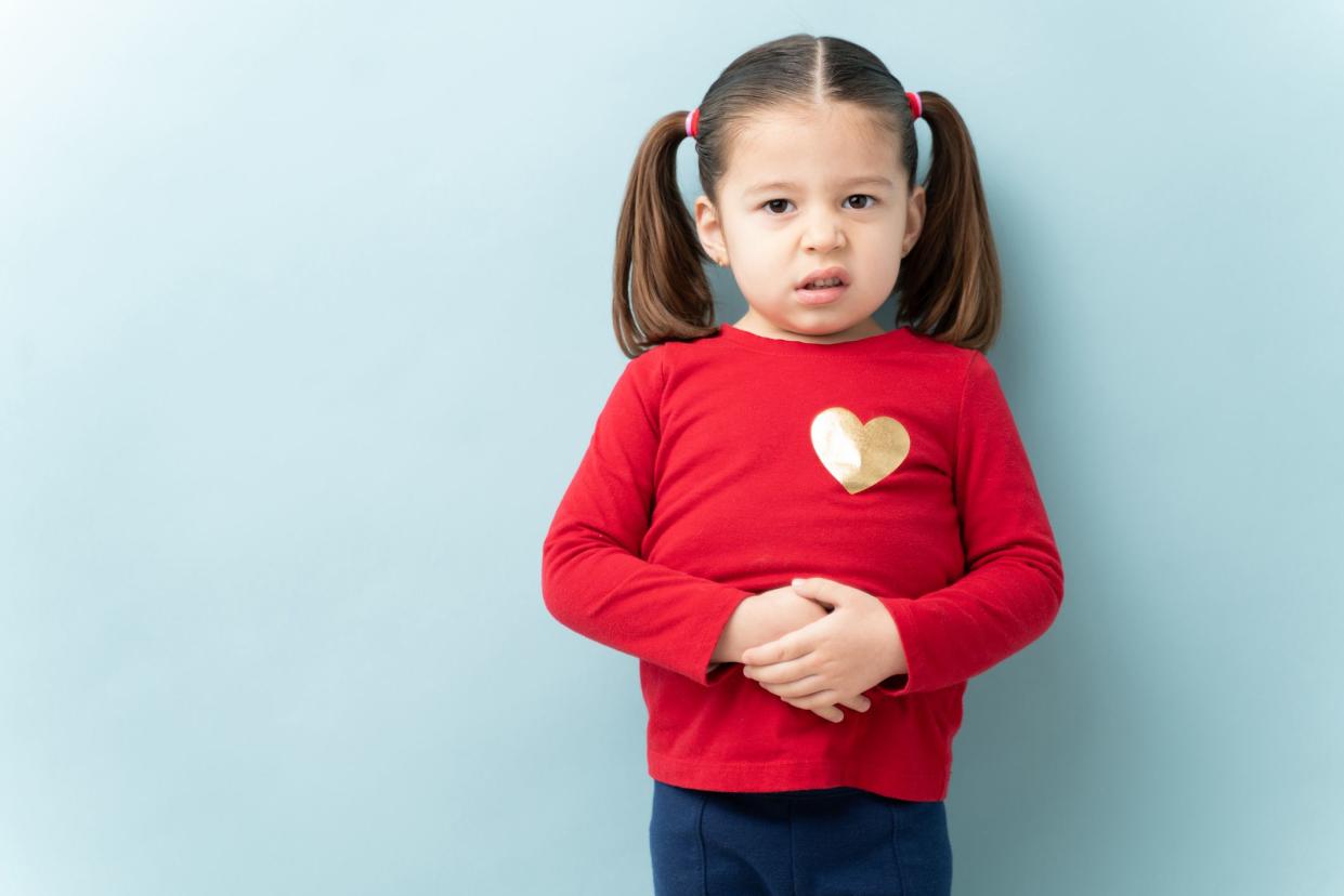 Serious looking little girl touching her belly and feeling sick with a stomachache in a studio