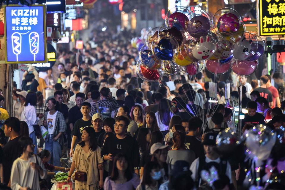 In this photo taken on September 8, 2020, a balloon seller walks among other pedestrians in a crowded street surrounded by small shops in the city of Changsha, China's Hunan province.