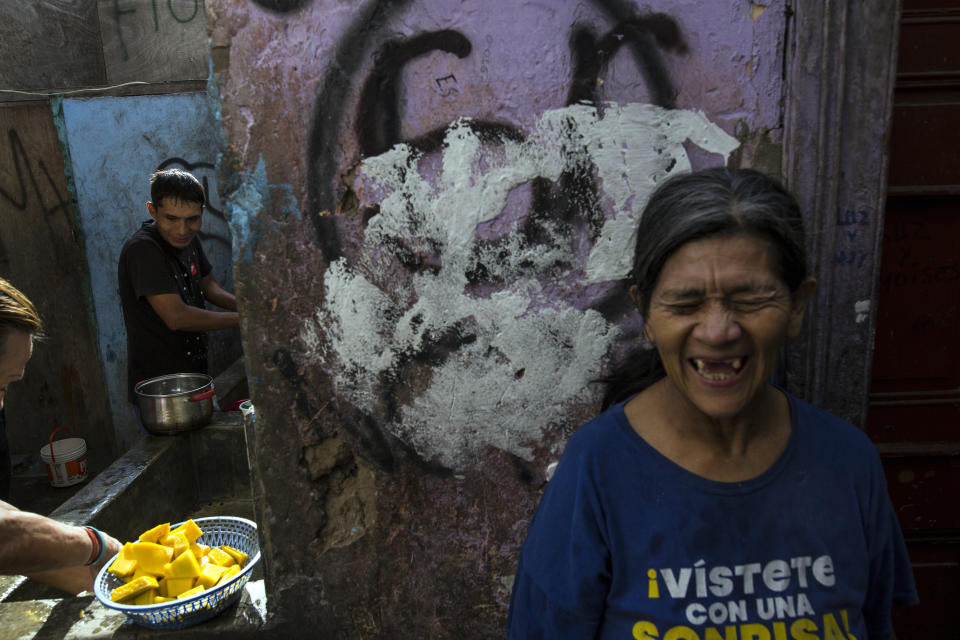 In this March 19, 2020 photo, Nelida Rojas, wearing a T-shirt emblazoned with a message that reads in Spanish: "Dress yourself with a smile", laughs as she jokes with fellow residents as she waits her turn to use the communal laundry area, inside a rundown building nicknamed "Luriganchito" after the country's most populous prison, in Lima, Peru. Rojas, 59, had a stroke two years ago that partially paralyzed her body. She now uses crutches to get around and spends her days begging for alms. (AP Photo/Rodrigo Abd)