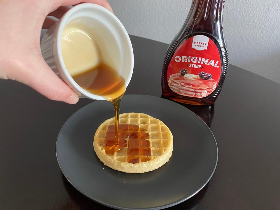 hand pouring white ramekin filled with market pantry syrup onto a frozen waffle