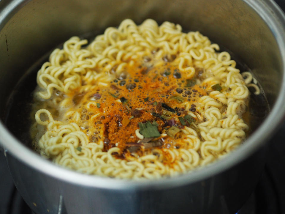 ramen noodles cooking in a pot with seasoning on top