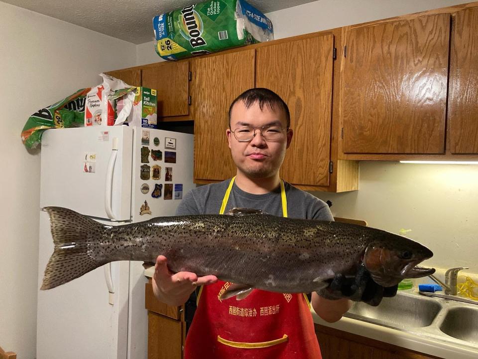 Liu He holds a steelhead in his home in West Lafayette. He won 15 Fish of the Year awards from the Indiana Department of Natural Resources in 2022. Liu will try eating every species at least once to see how it tastes.