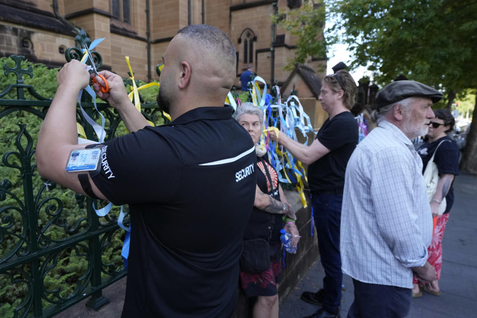 A security guard removes ribbons left by protesters as a symbol of support to sex abuse victims tied to a fence at St. Mary's Cathedral where Cardinal George Pell's coffin will be brought to lay in state in Sydney, Wednesday, Feb. 1, 2023. Pell, who was once considered the third-highest ranking cleric in the Vatican and spent more than a year in prison before his child abuse convictions were squashed in 2020, died in Rome last month at age 81. (AP Photo/Rick Rycroft)