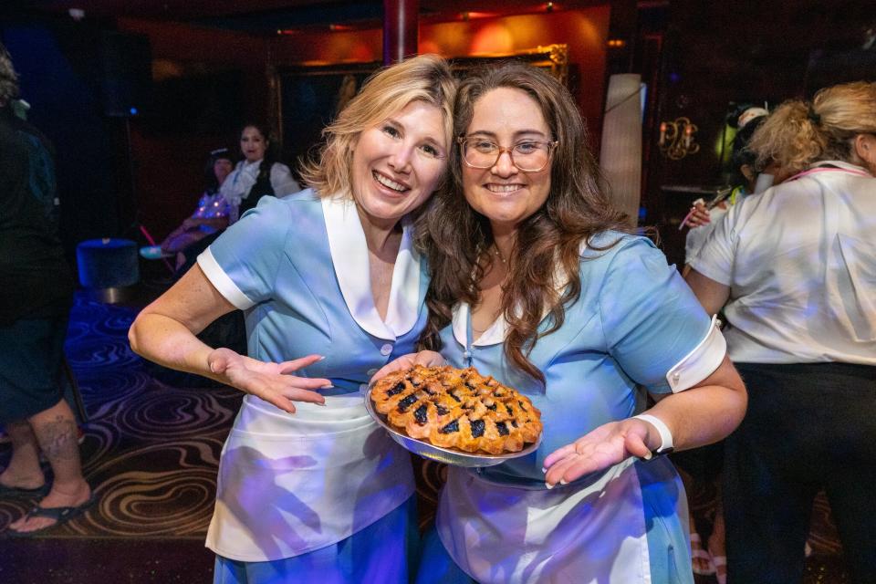 Two women dressed as waitresses and held a cake.