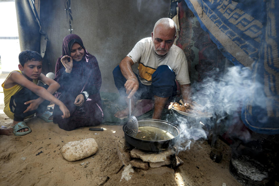 Hassan Nofal, right, who was displaced by the Israeli bombardment of the Gaza Strip, prepares lunch with his family at a makeshift tent camp in Khan Younis, southern Gaza Strip, Thursday, July 4, 2024. Over nine months of war between Israel and Hamas, Palestinian families in Gaza have been uprooted repeatedly, driven back and forth across the territory to escape the fighting. Each time has meant a wrenching move to a new location and a series of crowded, temporary shelters. (AP Photo/Abdel Kareem Hana)