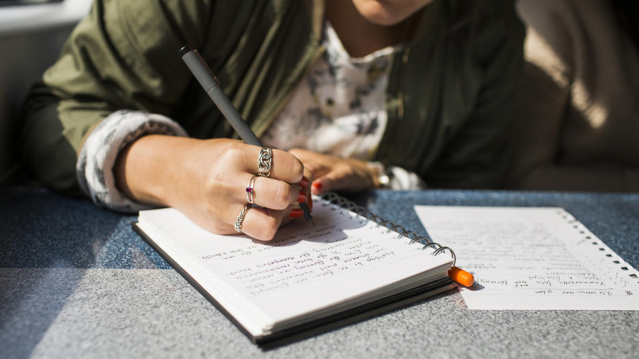 A person wearing three rings uses a pen to write in a journal