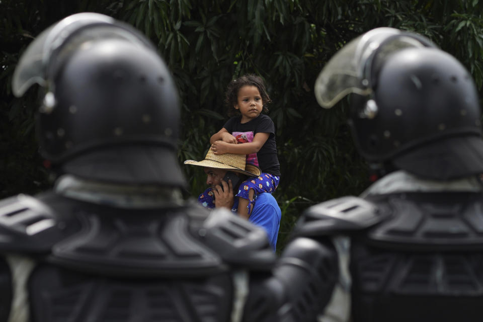 A man carries a child past members of the Mexican National Guard, on their way north on the Huixtla road in Chiapas state, Mexico, Wednesday, June 7, 2022. The group, part of a larger migrant caravan, left Tapachula on Monday, tired of waiting to normalize their status in a region with little work and still far from their ultimate goal of reaching the United States. (AP Photo/Marco Ugarte)