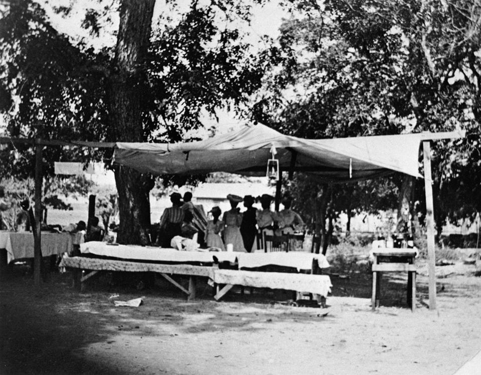 People and picnic tables under a tent in the park near "East Woods" on East 24th Street. Mrs. Grace Murray Stephenson, the photographer, kept a diary of the day's events, which she later sold to the San Francisco Chronicle which wrote a full-page feature on it.