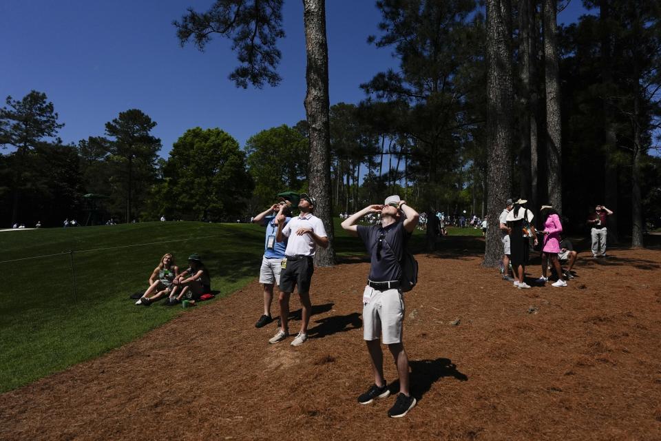 Patrons looks up at the sun during an solar solar eclipse during a practice round in preparation for the Masters golf tournament at Augusta National Golf Club Monday, April 8, 2024, in Augusta, Ga. (AP Photo/Ashley Landis)