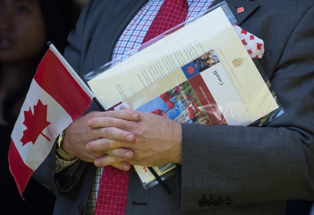A new Canadian holds a Canadian flag, their citizenship certificate and a letter signed by Prime Minister Justin Trudeau as they sing O Canada after becoming a Canadian citizen during a citizenship ceremony in West Vancouver on Monday, July 1, 2019. (Darryl Dyck/The Canadian Press - image credit)