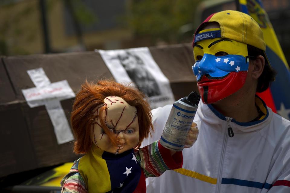 A protester with a Guy Fawkes mask, painted with the Venezuelan flag colors, carries a doll with a tear gas canister during a march of remembrance for those fallen during the protests in Caracas, Venezuela, Tuesday, April. 15, 2014. As Venezuela’s opposition is resuming negotiations with the government doubts are arising that the talks will produce a breakthrough. (AP Photo/Ramon Espinosa)(AP Photo/Ramon Espinosa)