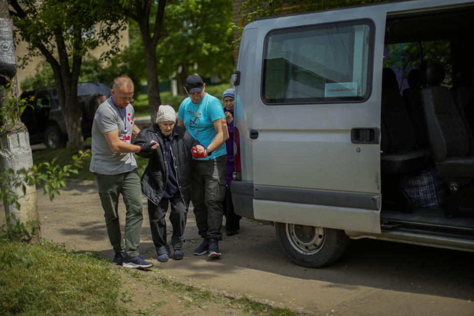 Roman Zhylenkov, left, and another volunteer of Vostok SOS charitable organisation help an elderly woman during an evacuation in Kramatorsk, eastern Ukraine, Thursday, May 26, 2022. Volunteer drivers are risking everything to deliver humanitarian aid to Ukrainians behind the front lines of the war — and to help many of them escape. The routes are dangerous and long and the drivers risk detention, injury or death. (AP Photo/Francisco Seco)