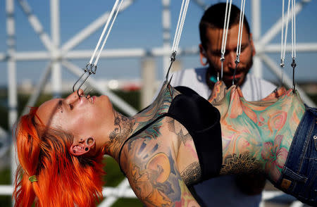 Professional body artist Dino Helvida (R), 27, inspects Kaitlin, 28, from the United States, as she is suspended from hooks pierced through her skin in Zagreb, Croatia June 7, 2016. REUTERS/Antonio Bronic