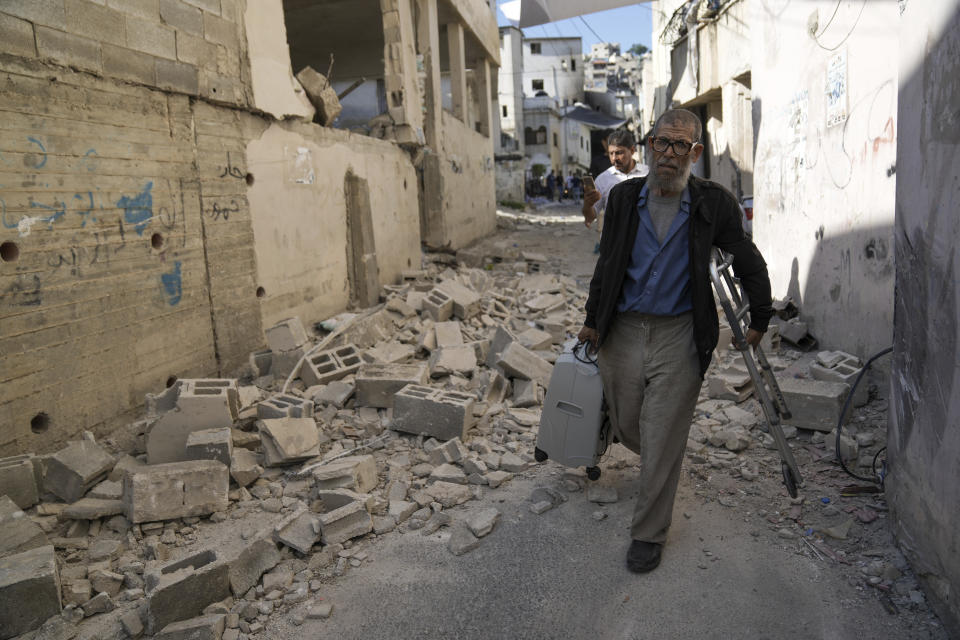 Palestinians walk by a damaged house in the Jenin refugee camp in the West Bank, Wednesday, July 5, 2023, after the Israeli army withdrew its forces from the militant stronghold. The withdrawal of troops from the camp ended an intense two-day operation that killed at least 13 Palestinians, drove thousands of people from their homes and left a wide swath of damage in its wake. One Israeli soldier was also killed. (AP Photo/Nasser Nasser)