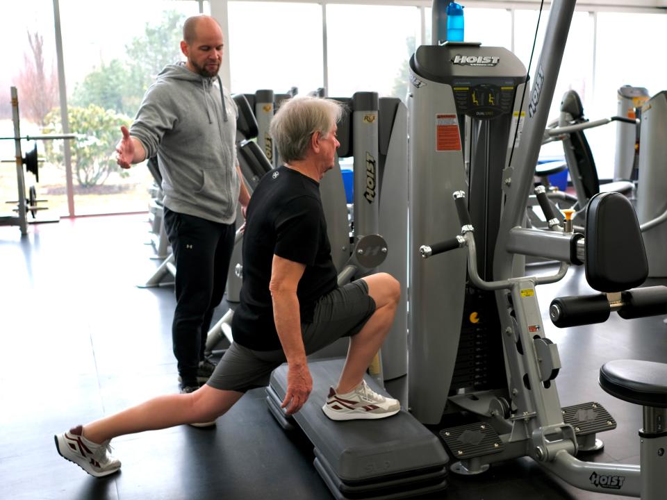 Barry does a lunge in the gym while his personal trainer coaches him.