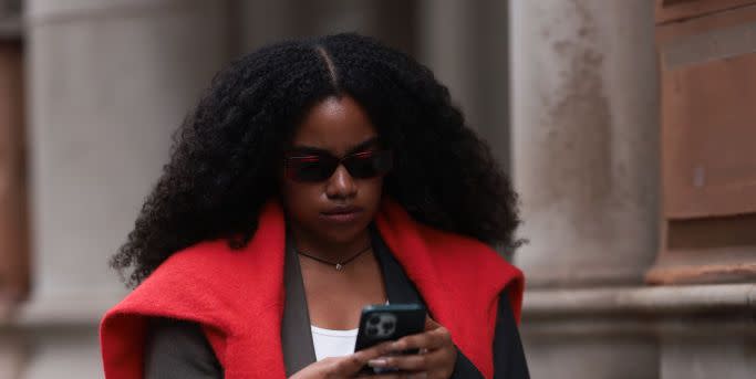 a girl at london fashion week wearing a red jumper over a blazer and a white top whilst on her phone