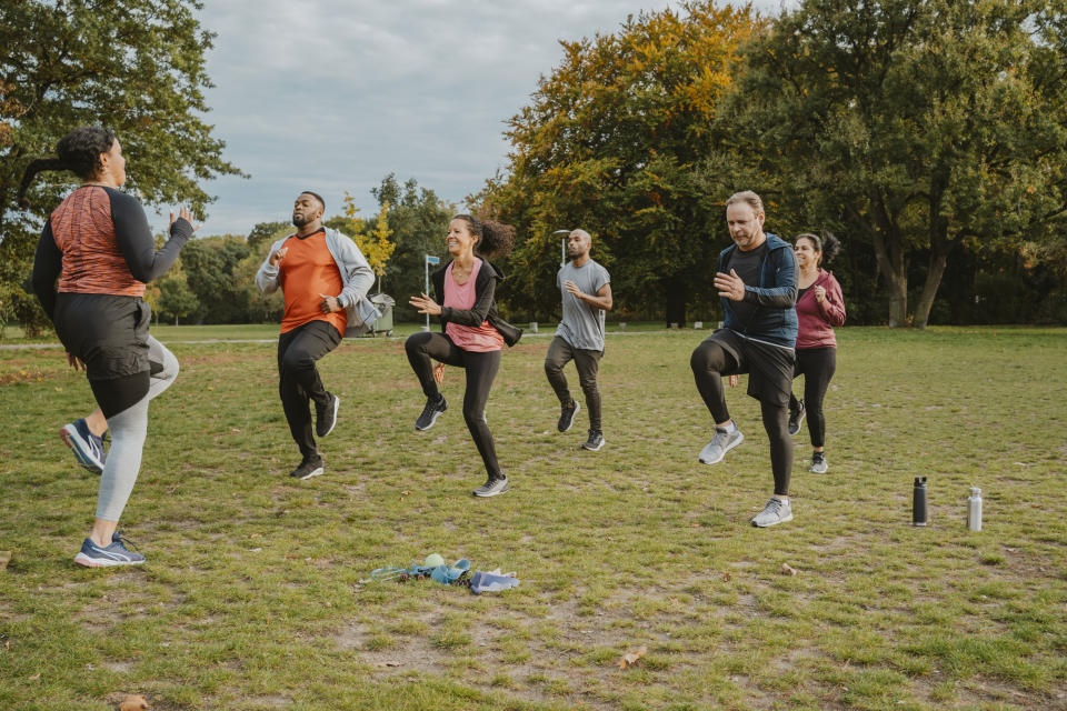 Group of people doing high-knee exercises in a park with a trainer