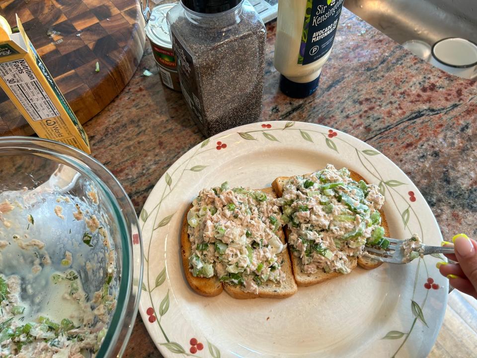 A tuna mixture being spread onto two slices of bread with a fork.
