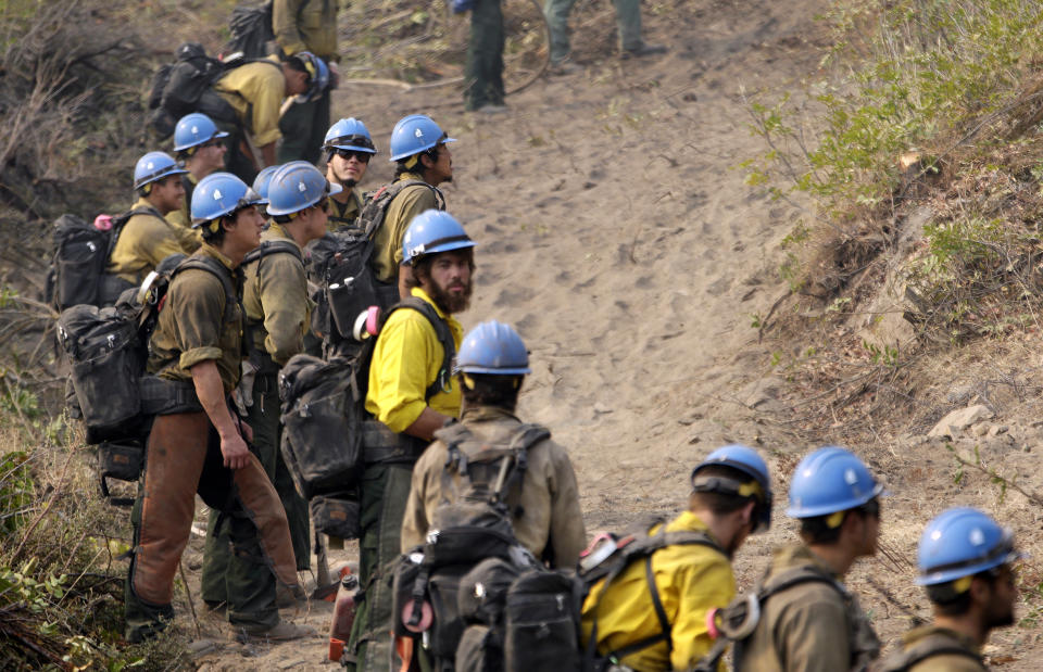 FILE - In this Aug. 27, 2015 file photo firefighters from the University of Alaska (Fairbanks) watch as a wildfire slowly creeps toward their fire break near Chelan, Wash. Newly released national plans for fighting wildfires during the coronavirus pandemic are hundreds of pages long but don't offer many details on how fire managers will get access to COVID-19 tests or exactly who will decide when a crew needs to enter quarantine. (AP Photo/Elaine Thompson,File)