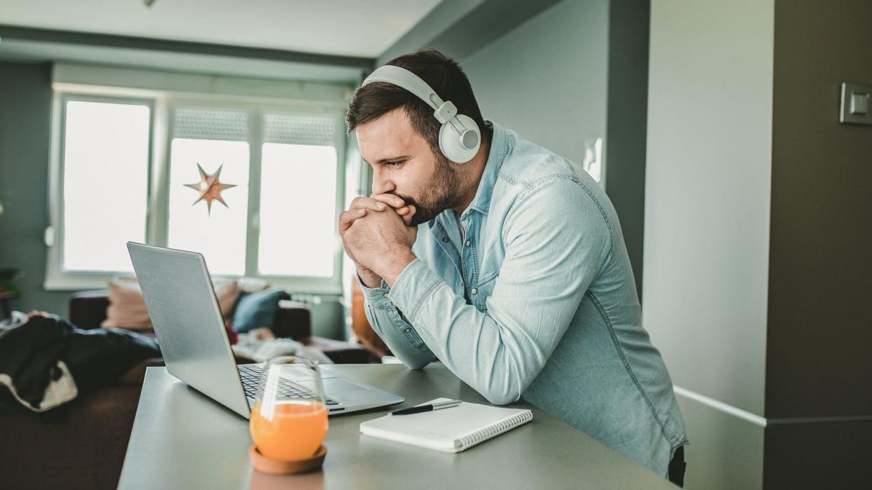 Young man is at home, with headphones and watching a online course.