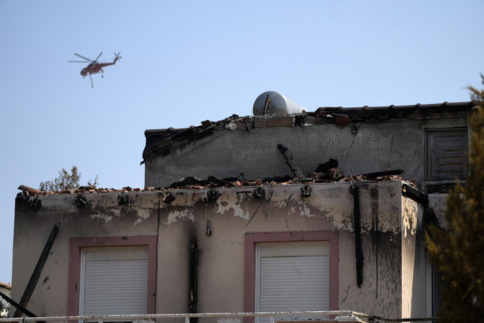 A helicopter flies near a house with a burnt roof during a wildfire on Mount Parnitha, in northwestern Athens, Greece, Thursday, Aug. 24, 2023. A major wildfire burning on the northwestern fringes of the Greek capital has torched homes and is now threatening the heart of a national park of Parnitha, one of the last green areas near the Greek capital. (AP Photo/Thanassis Stavrakis)