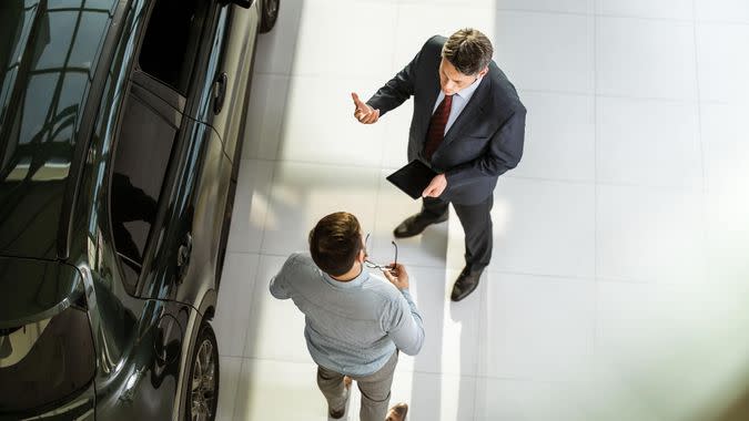High angle view of a salesperson using touchpad while talking to his male customer in a car showroom.