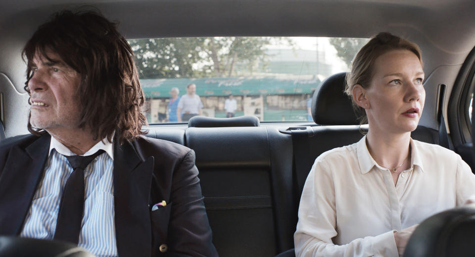 Peter Simoniskchek and Sandra Huller sit in the backseat of a car and look out opposite windows