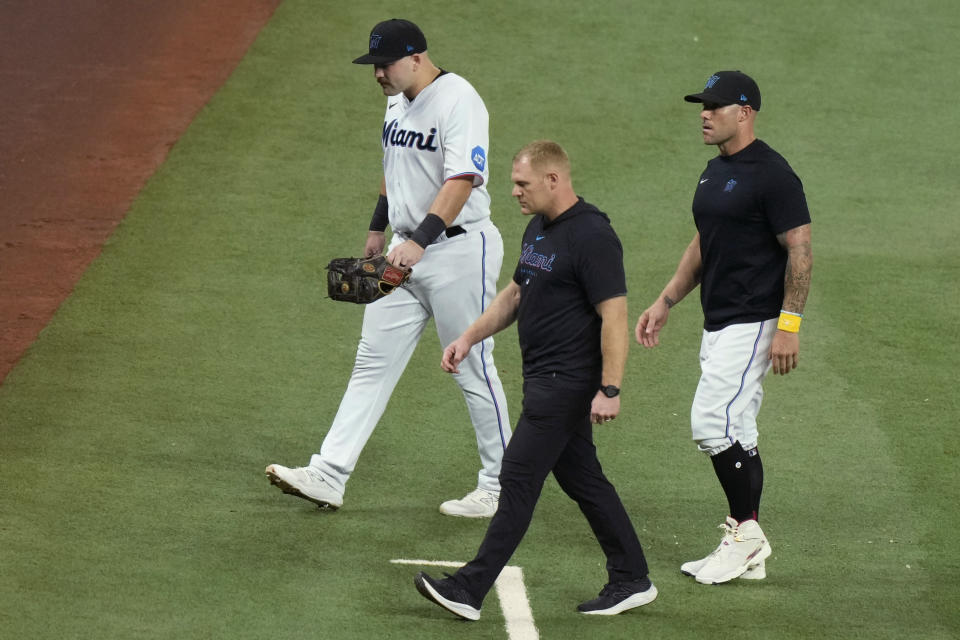 Miami Marlins third baseman Jake Burger, left, walks off the field after an injury during the third inning of the team's baseball game against the New York Mets, Wednesday, Sept. 20, 2023, in Miami. At right is Marlins manager Skip Schumaker. (AP Photo/Lynne Sladky)