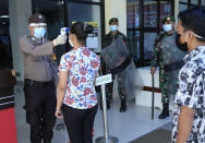 A police officer takes the temperature reading of a visitor as soldiers equipped with riot gears who are stationed at Bhayangkara Hospital following an incident where mob forcefully took the body of a man who presumably died of COVID-19 look on, in Makassar, South Sulawesi, Indonesia, Sunday, June 21, 2020. As Indonesia’s virus death toll rises, the world’s most populous Muslim country finds itself at odds with protocols put in place by the government to handle the bodies of victims of the pandemic. This has led to increasing incidents of bodies being taken from hospitals, rejection of COVID-19 health and safety procedures, and what some experts say is a lack of communication from the government. (AP Photo/Masyudi Syachban Firmansyah)