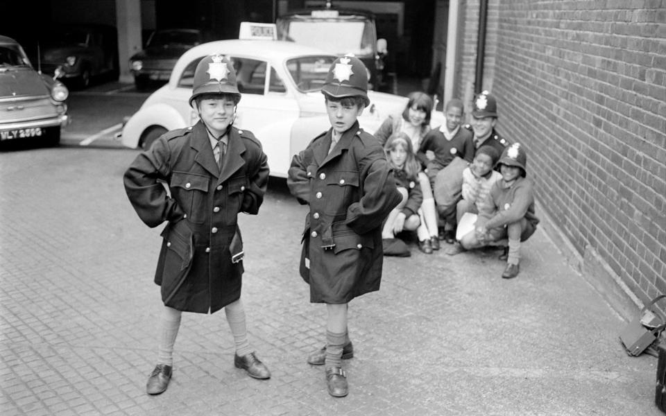 Today they went to the Tooting Police Station, where P.C. Brian Curson of Wandsworth showed them around, they have become his group and come to him for advice, but primarily they run the club themselves. Year old twins Peter and Nigel Nethercote try on new policeman's uniforms which had just arrived at the station. In the background P.C. Curson and the other children. October 1969 Z10506-001 (Photo by Mirrorpix/Mirrorpix via Getty Images) - Getty