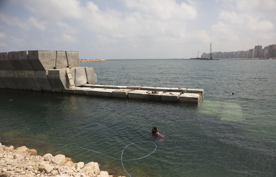 In this Aug. 8, 2019 photo, a worker in diving gear prepares to place cement blocks to stave off rising water levels near the corniche in Alexandria, Egypt. Alexandria, which has survived invasions, fires and earthquakes since it was founded by Alexander the Great more than 2,000 years ago, now faces a new menace from climate change. Rising sea levels threaten to inundate poorer neighborhoods and archaeological sites, prompting authorities to erect concrete barriers out at sea to hold back the surging waves. (AP Photo/Maya Alleruzzo)
