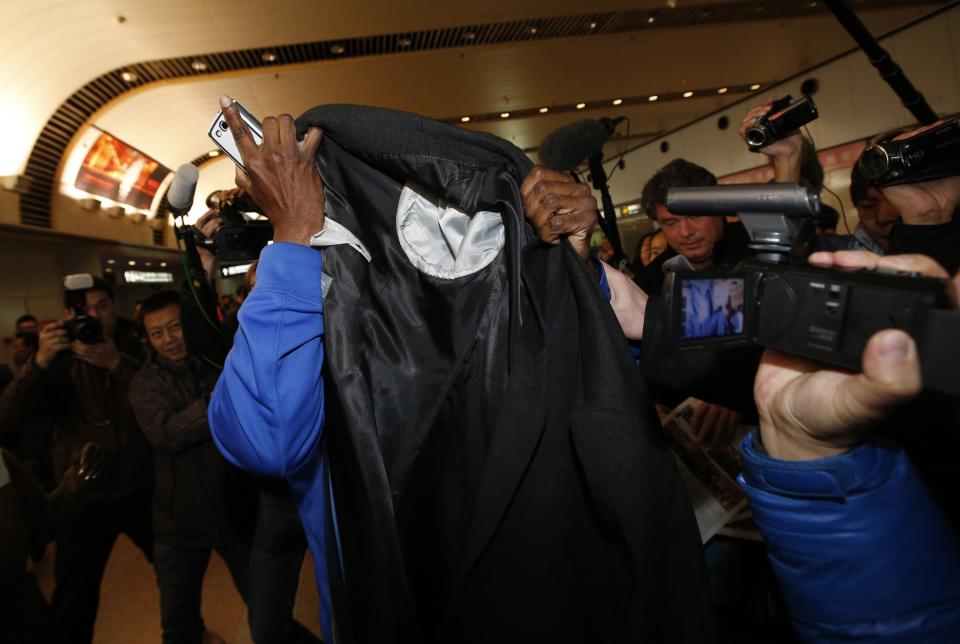 Former NBA basketball player Eric "Sleepy" Floyd covers his face with clothes as journalists chase him upon his arrival from North Korea's Pyongyang, at Beijing Capital International Airport