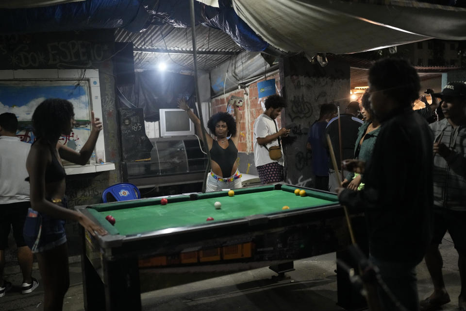 A woman stretches at a bar holding the Gas Battle rapping competition in the City of God favela of Rio de Janeiro, Brazil, late Wednesday, Nov. 10, 2021. Rap artists in the favela are starting to compete again since the COVID-19 pandemic curtailed public gatherings, presenting local residents with a show in a sign of a return to normalcy for music lovers. (AP Photo/Silvia Izquierdo)