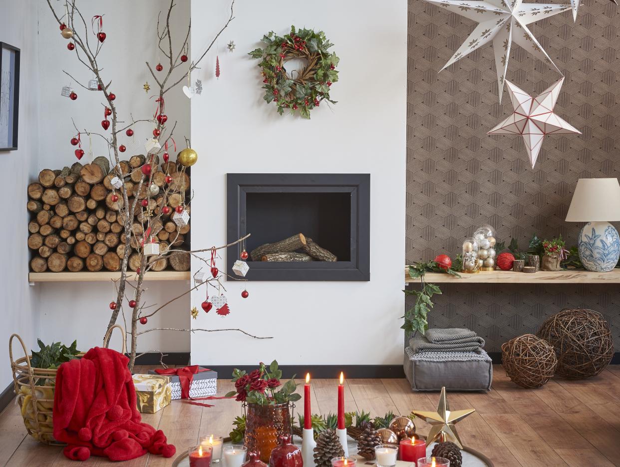  A living room decorated for Christmas with a decorated twig tree, a stack of firewood, and hanging paper star shades. 