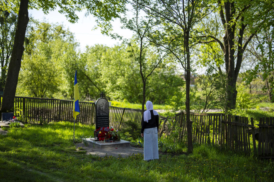 Local resident Liudmyla Havryliuk stands next to a memorial stone that commemorates six Ukrainian soldiers killed by Russians, in the yard of the Church of the Intercession of the Blessed Virgin Mary in, Lypivka, near Lviv, Ukraine, Sunday, April 28, 2024. This Orthodox Easter season, an extraordinary new church is bringing spiritual comfort to war-weary residents of the Ukrainian village of Lypivka. Two years ago it also provided physical refuge from horrors outside. (AP Photo/Francisco Seco)