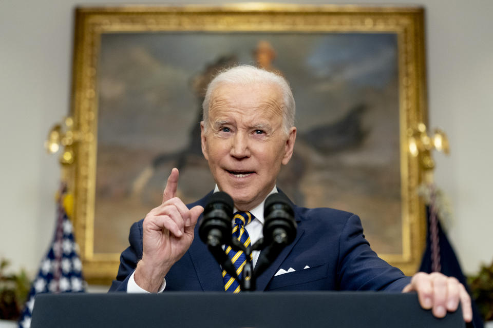 President Biden raises a finger in warning in the White House as he speaks into a microphone in front of a large oil of a cowboy