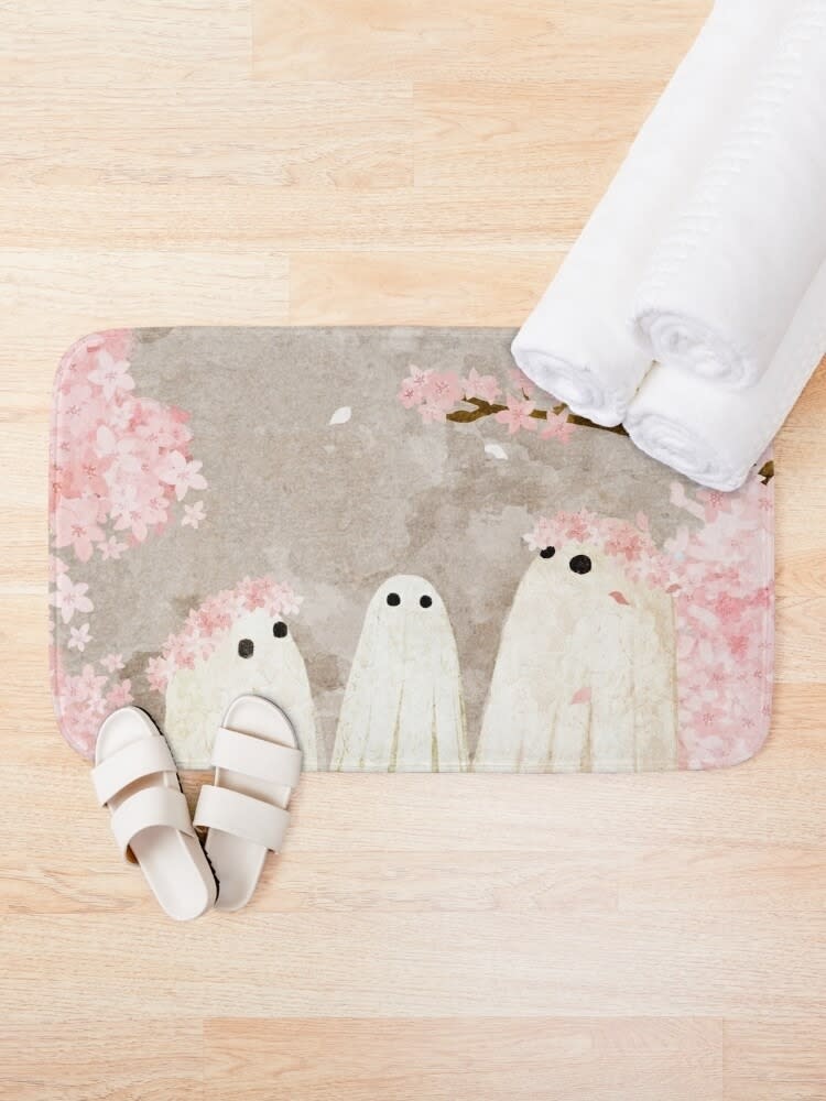 Patterned bath mat with cartoon ghosts, beside rolled towels and slippers. Used for cozy bathroom decor ideas