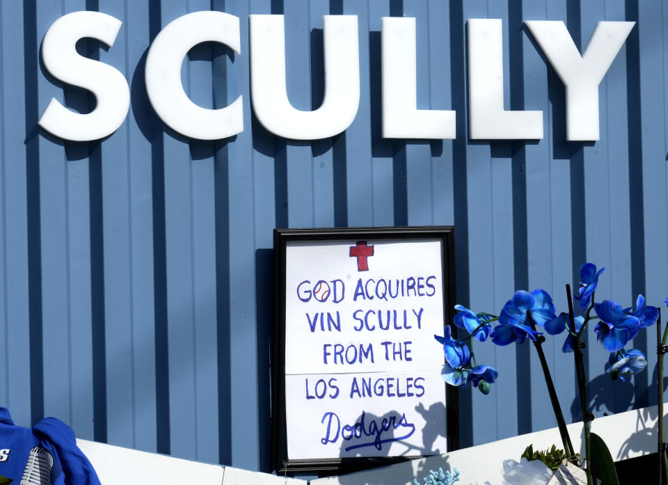 A framed not, "God Acquires Vin Scully From the Los Angeles Dodgers," is part of a growing makeshift memorial to Scully in front of the Welcome to Dodger Stadium sign along Vin Scully Avenue in Los Angeles on Wednesday, Aug. 3, 2022. Scully, whose 67-year career calling games in Brooklyn and Los Angeles made him the longest-tenured broadcaster with a single team in sports history, died Tuesday night at age 94. (Keith Birmingham/The Orange County Register via AP)
