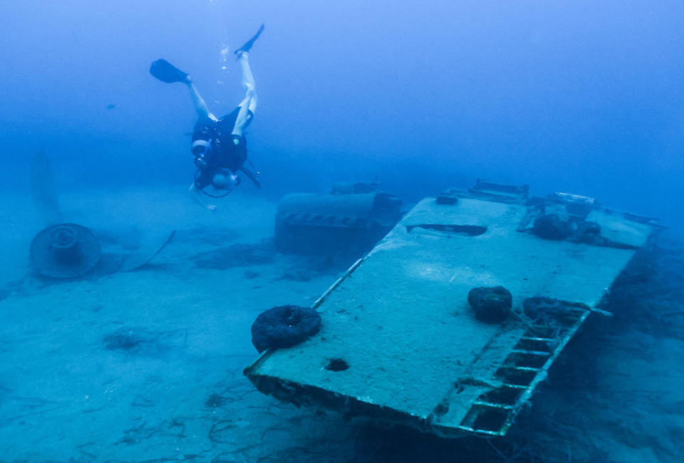 A diver swims toward a hunk of metal on the sea floor