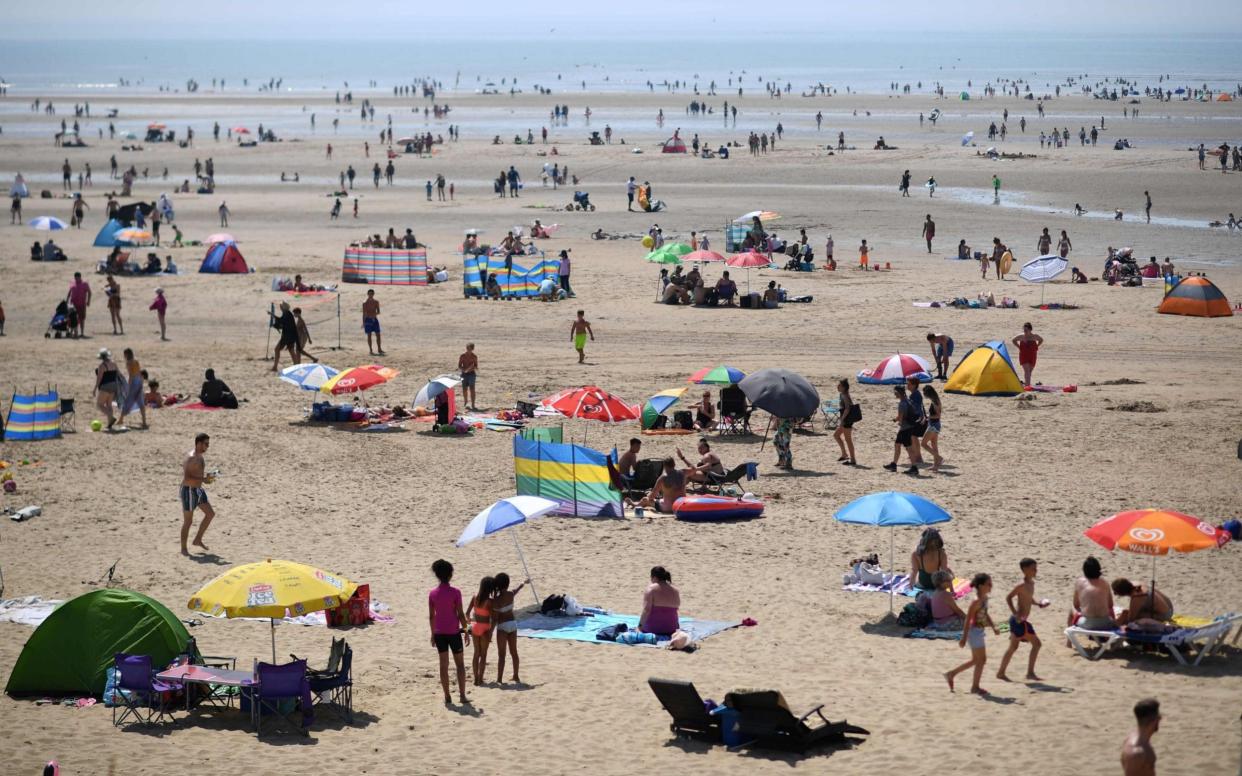 Beach-goers enjoy the sunshine by the sea in Camber Sands, southern England, during a heatwave in Britain earlier this summer - AFP