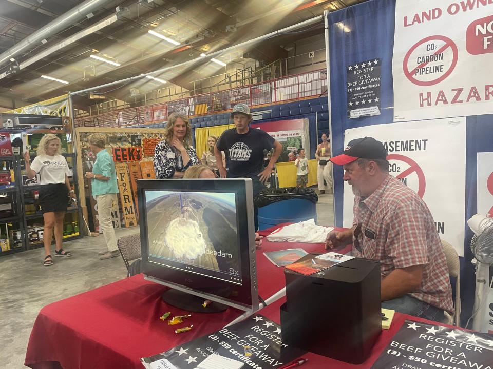 Bruce Mack of Leola visits with a woman at the Brown County Fair about his concerns about the use of eminent domain by Summit Carbon Solutions and its proposed carbon dioxide pipeline. On the television screen is a video of a simulated CO2 pipeline breach in the United Kingdom.