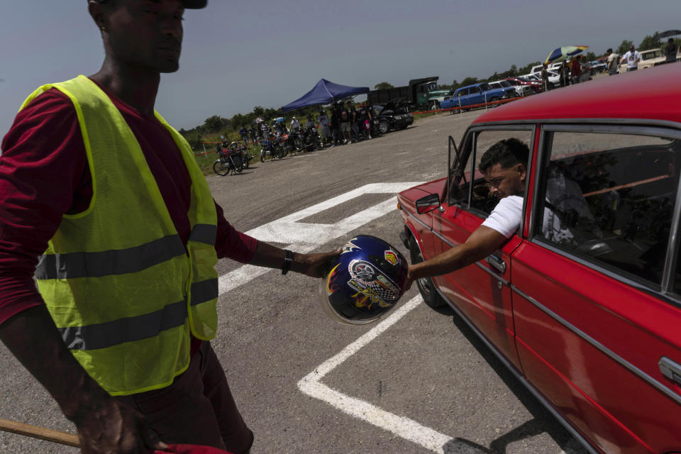 El juez de carreras de resistencia entrega un casco obligatorio a un piloto de Lada en una pista de aterrizaje vieja y sin uso en San Nicolás de Bari, Cuba, el domingo 23 de julio de 2023. (Foto AP/Ramón Espinosa)