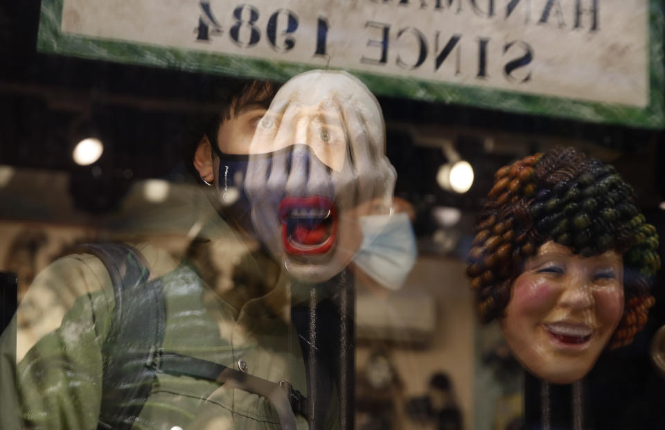 A young man looks at carnival masks reflected in the window of a shop in Venice, Italy, Saturday, Jan. 30, 2021. Last year, with fear over the new coronavirus mounting, authorities abruptly shut down Venice Carnival on its third day, just before Italy became the first country in the West facing a outbreak. (AP Photo/Antonio Calanni)