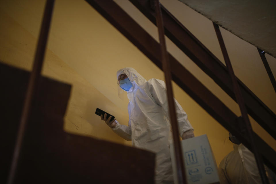 In this Friday, May 15, 2020 photo, a contact tracer with Turkey's Health Ministry's coronavirus contact tracing team, clad in white protective gear, mask and face shield, arrives at the house in Istanbul of Betul Sahbas, who had been experiencing COVID-19 symptoms, to take a sample. Teams of contact tracers in Istanbul, the epicenter of the pandemic in Turkey and its most populous city, and also nationwide, are going house to house to test people experiencing COVID-19 symptoms and inform patients on isolation. (AP Photo/Emrah Gurel)