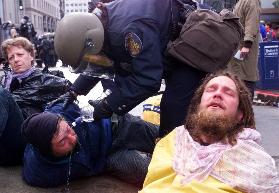 FILE - In this Nov. 30, 1999, file photo, a Seattle police officer uses water to rinse the eyes of protester after making an arrest during demonstrations against the World Trade Organization meetings in downtown Seattle. Saturday, Nov. 30, 2019 marks 20 years since tens of thousands of protesters converged on Seattle and disrupted a major meeting of the World Trade Organization. The protesters’ message was amplified not just by their vast numbers but by the response of overwhelmed police, who fired tear gas and plastic bullets and arrested nearly 600 people. Two decades later, many of their causes are still relevant. (AP Photo/Itsu Inouye, File)