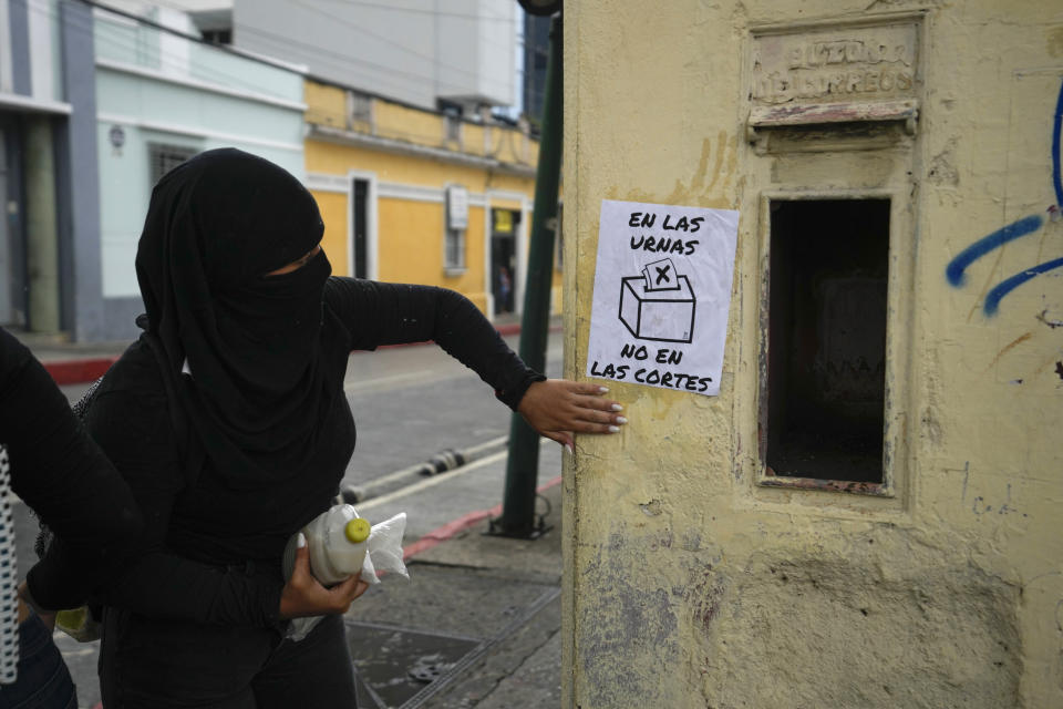 A demonstrator glues to a wall a sign with a message that reads in Spanish: "In the ballot boxes, not the courts," during a march to support the electoral process in Guatemala City, Saturday, July 8, 2023. Chief Justice Silvia Valdes Quezada issued an order blocking the certification of the results for the first-round presidential June 25th election, late Friday. (AP Photo/Moises Castillo)