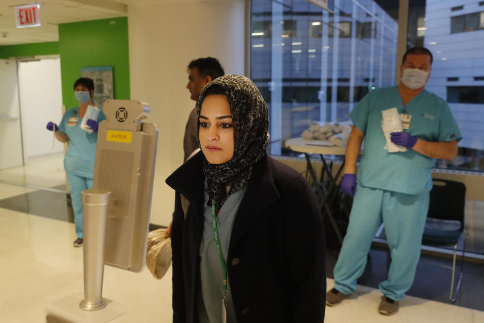 In this Wednesday, April 22, 2020, RUSH Hospital respiratory therapist Jumana Azam pauses before a face temperature scanner as she reports for her early morning shift at the hospital in Chicago. (AP Photo/Charles Rex Arbogast)